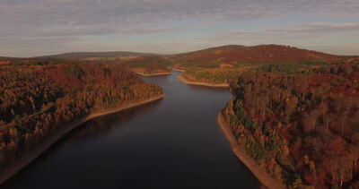 Luftaufnahme einer Talsperre im goldenen Herbstwald bei Sonnenuntergang