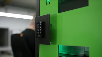 Zahlencode Tastatur an einer grünen Industriemaschine mit Mitarbeiter im Hintergrund