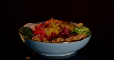 Herzhafte Bowl mit roter Sauce Edamame und Kartoffelspalten vor dunklem Hintergrund