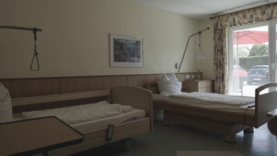 Leeres Pflegezimmer mit Pflegebett und Aufrichthilfe am Fenster