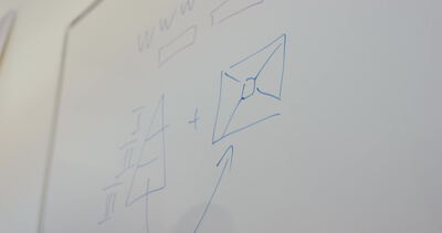 Hand zeichnet eine geometrische Formel mit blauem Marker auf ein Whiteboard