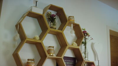 Sechseckige Holzregale mit Blumen und Honiggläsern an der Wand