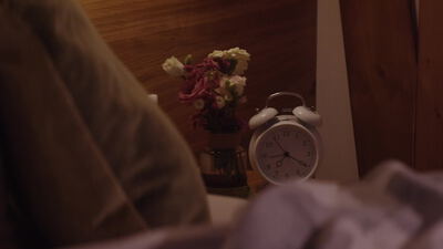 Analoger Wecker und Blumen auf dem Nachttisch im Schlafzimmer
