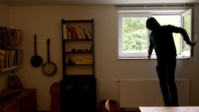 Einbrecher steigt durch ein offenes Fenster in ein Wohnzimmer, Einbrecher Fenster, Einbruch durch Fenster und Einbrecher