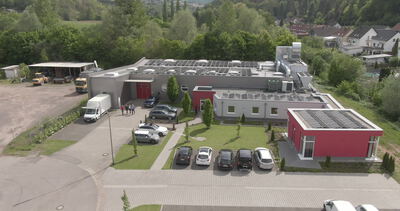 Betriebsgebäude mit Solardach und Parkplatz im Grünen von oben