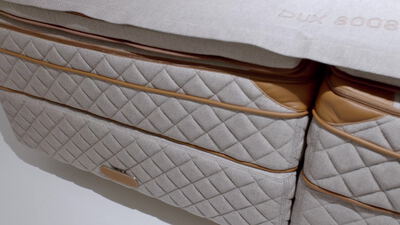 Luxuriöses Boxspringbett mit grauer Polsterung und goldener Paspel
