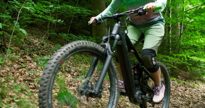 Frau fährt Mountainbike auf schmalem Waldpfad im grünen Wald