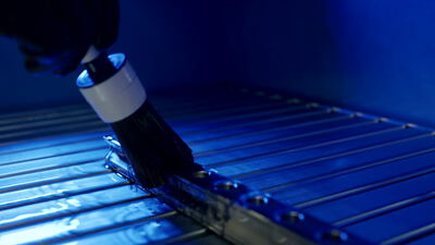 Behandschuhte Hand führt einen Applikator über eine Metallschiene