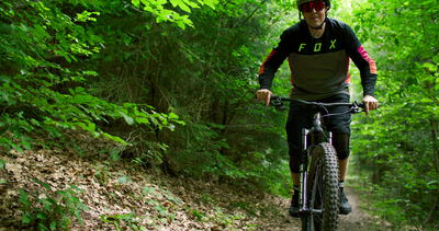 Mann fährt mit dem Mountainbike frontal auf die Kamera zu im Wald