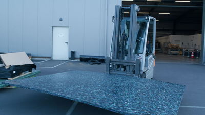 Gabelstapler transportiert recycelte Gummimatte vor Industriehalle