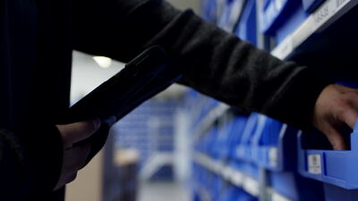 Handscanner vor blauen Lagerboxen bei der Kommissionierung im Lager