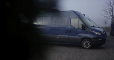 Dunkelblauer Lieferwagen steht im Nebel auf gepflastertem Hof