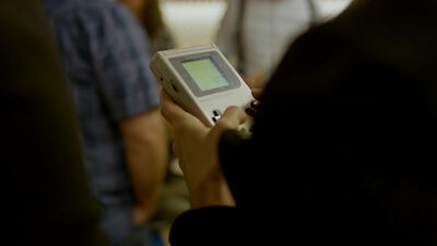 Hände halten eine graue Retro Spielekonsole mit grünem Bildschirm