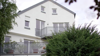 Modernes weißes Wohnhaus mit Balkon und Satteldach hinter Bäumen