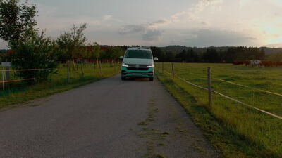 Türkiser Campingbus fährt bei Sonnenuntergang über eine Landstraße