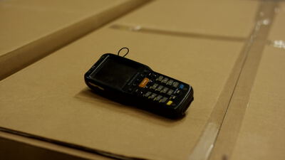 Mobiler Handscanner liegt auf gestapelten Kartons im warmen Licht