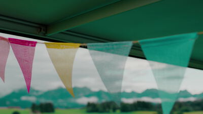 Bunte Wimpelkette weht unter einer grünen Markise vor Bergpanorama