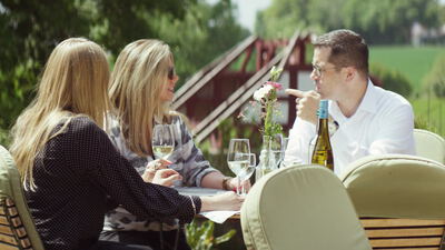 Freunde genießen Weißwein an einem sonnigen Gartentisch