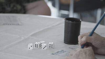 Ältere Menschen spielen ein Würfelspiel mit Würfelbecher am Tisch