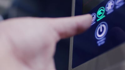 Finger bedient beleuchtetes Touchpanel einer Industriemaschine mit Start und Stopp Symbolen