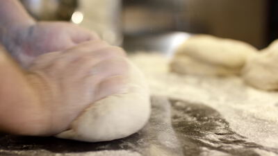 Bäckerhand formt runden Teigling auf bemehlter Arbeitsfläche