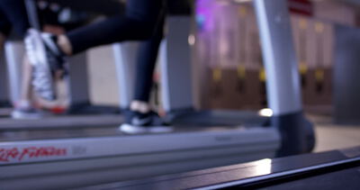 Füße laufen auf dem Laufband unter buntem Licht im Fitnessstudio