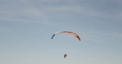 Gleitschirmflieger unter rot und weiß gefärbtem Schirm schwebt in den hellen Himmel Gleitschirmflieger unter rot und weiß gefärbtem Schirm schwebt in den hellen Himmel, Gleitschirmfliegen, Paragliding und