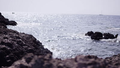 Felsküste mit glitzerndem Meer und Segelboot am Horizont
