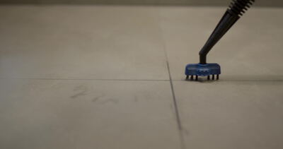 Dampfreiniger mit Bürstenaufsatz schrubbt Fugen im Fliesenboden