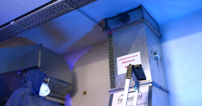 Arbeiter im Schutzanzug prüft ein Warnschild an einer Lüftungsanlage