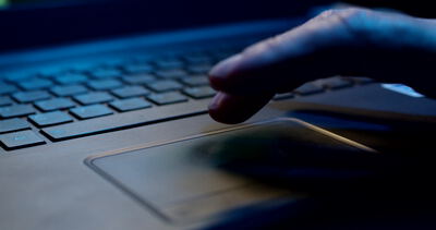 Finger bedient das Touchpad eines Laptops im blauen Licht