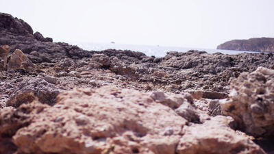 Felsige Küste mit glitzerndem Meer und ferner Insel am Horizont