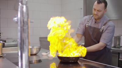 Koch flambiert ein Gericht mit Flammen in der Profiküche