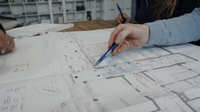 Hand mit Stift zeigt auf einen Architektur Bauplan am Tisch