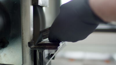 Behandschuhte Hand schleift eine Metallklinge an einer Maschine