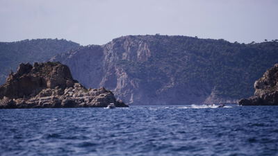 Ein Motorboot und ein Jetski fahren vor steilen Felsklippen über das blaue Meer
