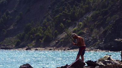 Angler steht mit der Rute auf den Felsen am türkisen Meer