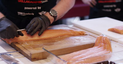 Frisches Lachsfilet wird mit Handschuhen auf einem Holzbrett zugeschnitten