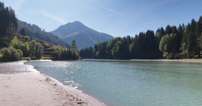 Sandufer an türkisfarbenem Wasser vor bewaldetem Berggipfel