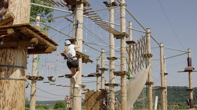 Junge Frau klettert im Hochseilgarten eines Kletterparks