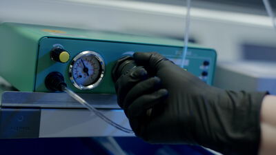 Hand im Handschuh bedient ein Messgerät mit Manometer und Display