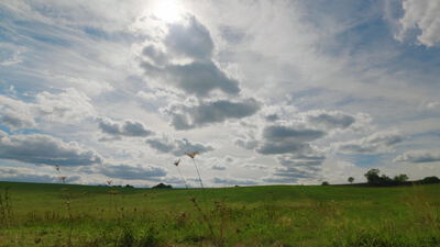 Weite Wiese unter großem Wolkenhimmel mit Sonne im Gegenlicht, großer Himmel, Wolkenhimmel über Wiese und Sonne hinter