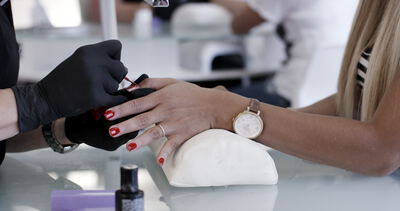 Nageldesignerin lackiert die Fingernägel einer Kundin mit rotem Nagellack im Nagelstudio