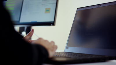 Hand zeigt am Arbeitsplatz auf Quellcode auf einem Computerbildschirm