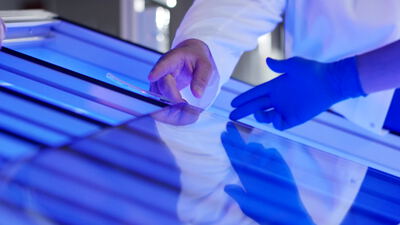 Haende pruefen eine geriffelte Glasplatte unter blauem Licht im Labor