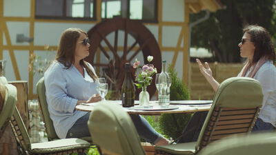 Zwei Frauen unterhalten sich bei Wein im Gartenlokal