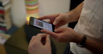 Mann scrollt Inhalte auf dem Smartphone in warmem Raum