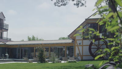 Wellnesshotel mit Wasserrad und Terrasse hinter grünen Blättern