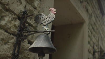Gusseiserne Wandglocke mit Hahn an einer alten Steinwand