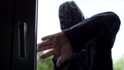 Vermummte Person greift von außen nach dem Griff einer Glastür